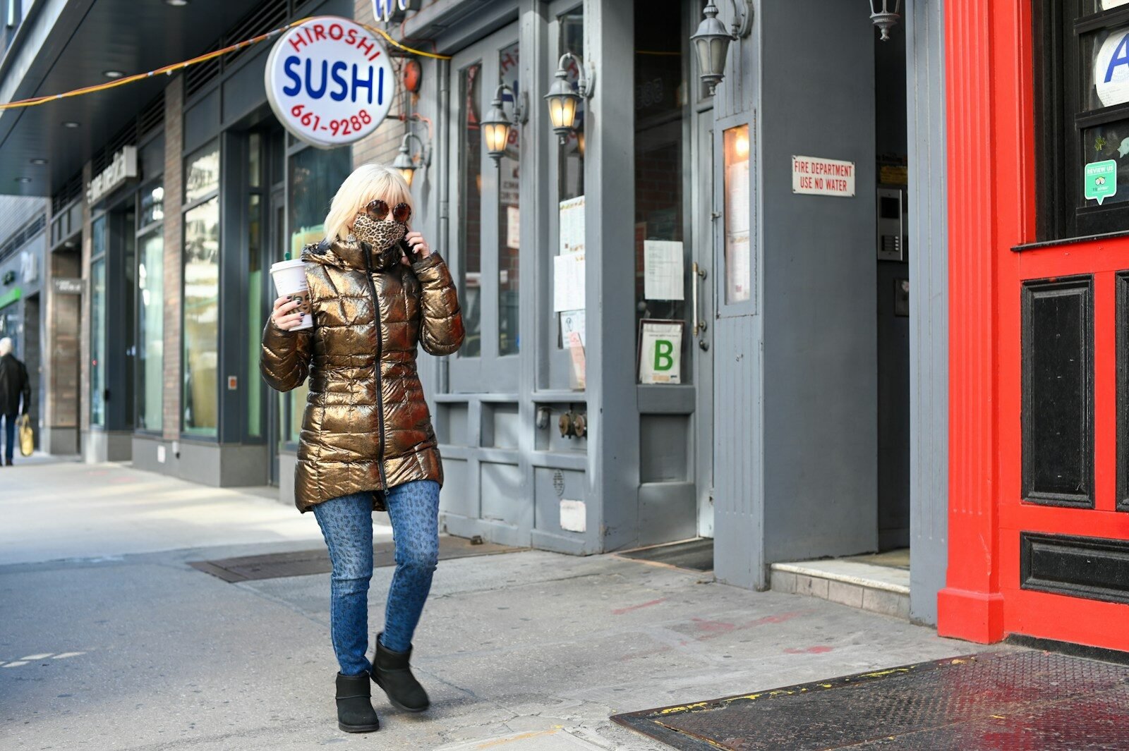 woman in brown jacket and blue denim jeans standing beside gray building during daytime